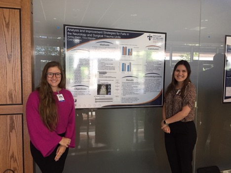 Two students posing with project board about hospital falls.