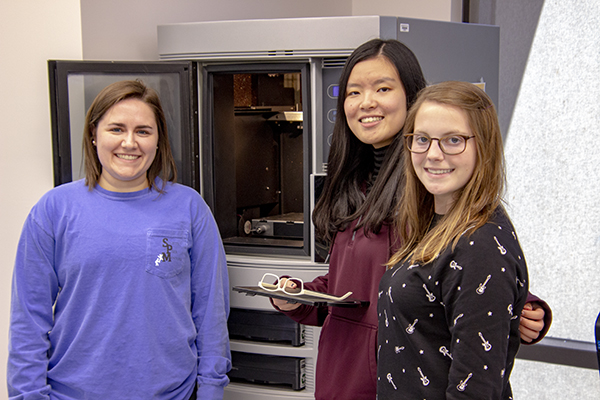 Three students posing by 3D printer