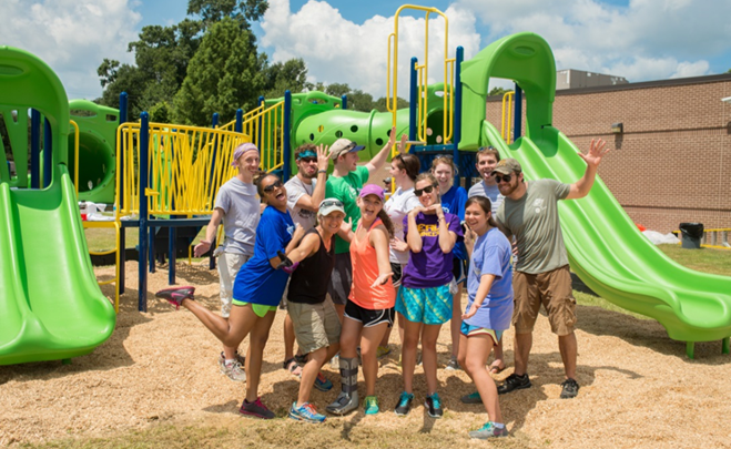 marybeth and her community playground project team pose together in front of a green and yellow playground build.