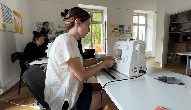 student uses sewing machine with others in background.