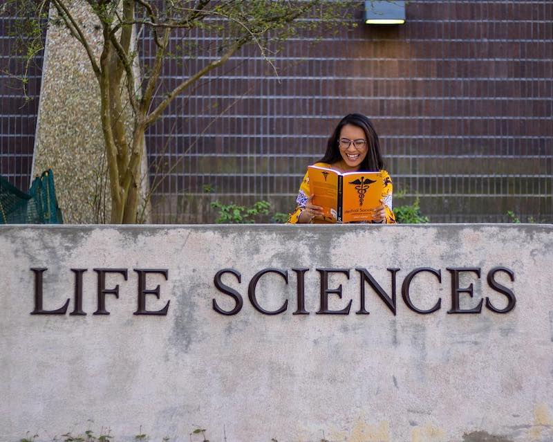 student reading a book in front of the LSU Life Sciences building