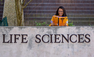 student Cindy Nguyen reading a book outside of the Life Sciences building