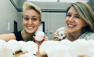 two female scientists posing for a selfie with 3D printed skull models
