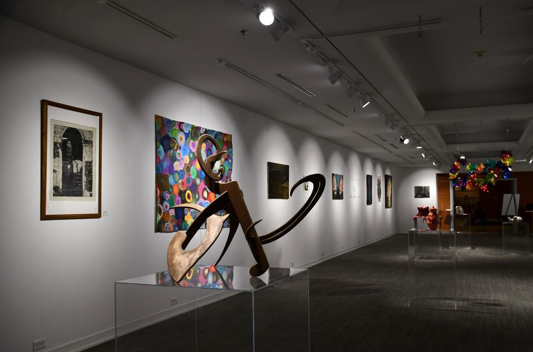 An outward view of the Art Gallery during a previous exhibit. gallery walls are lined with works and there are sculptures on pedestals.
