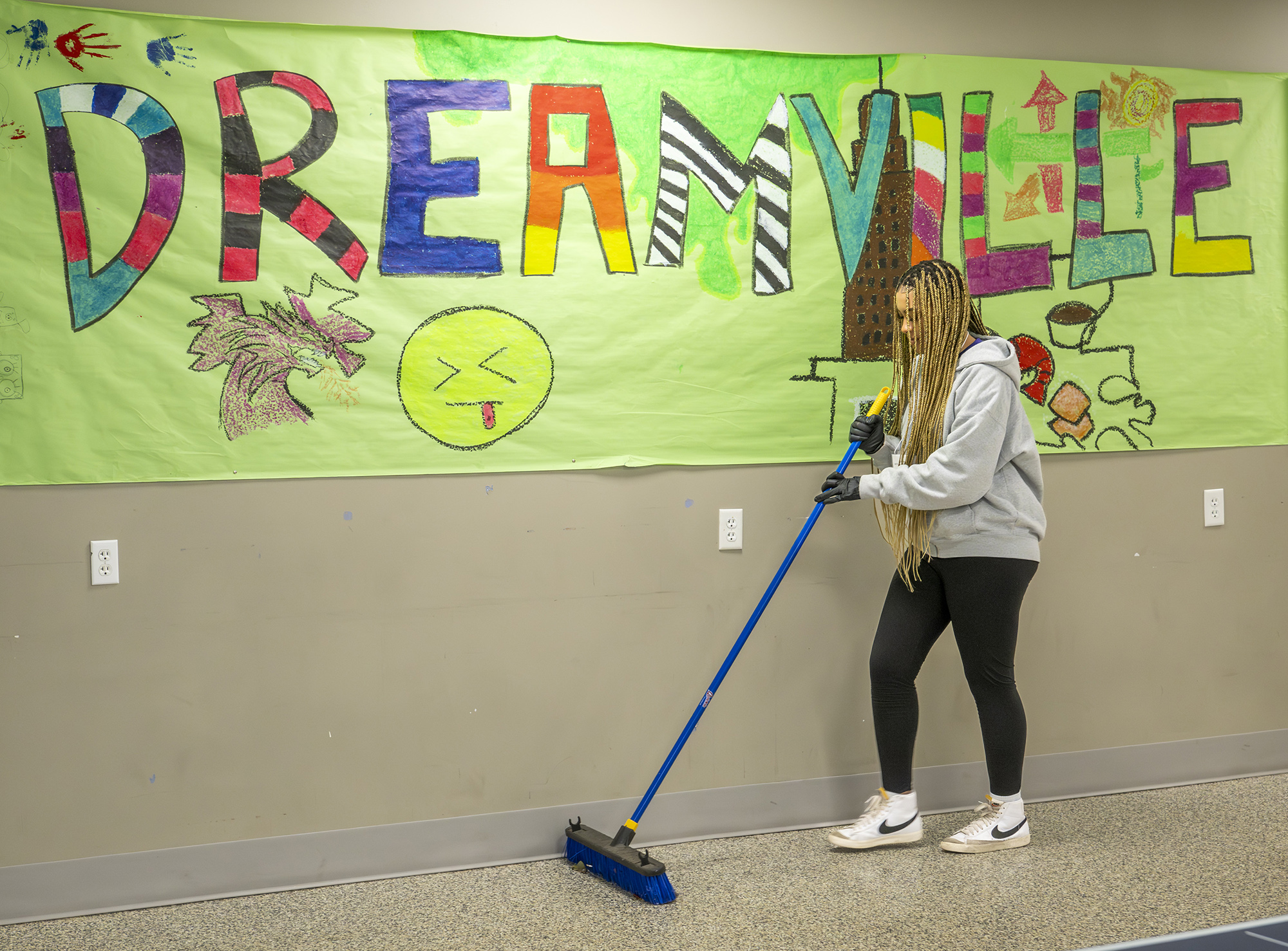Student sweeps the floor with a Dreamville banner iin the background.