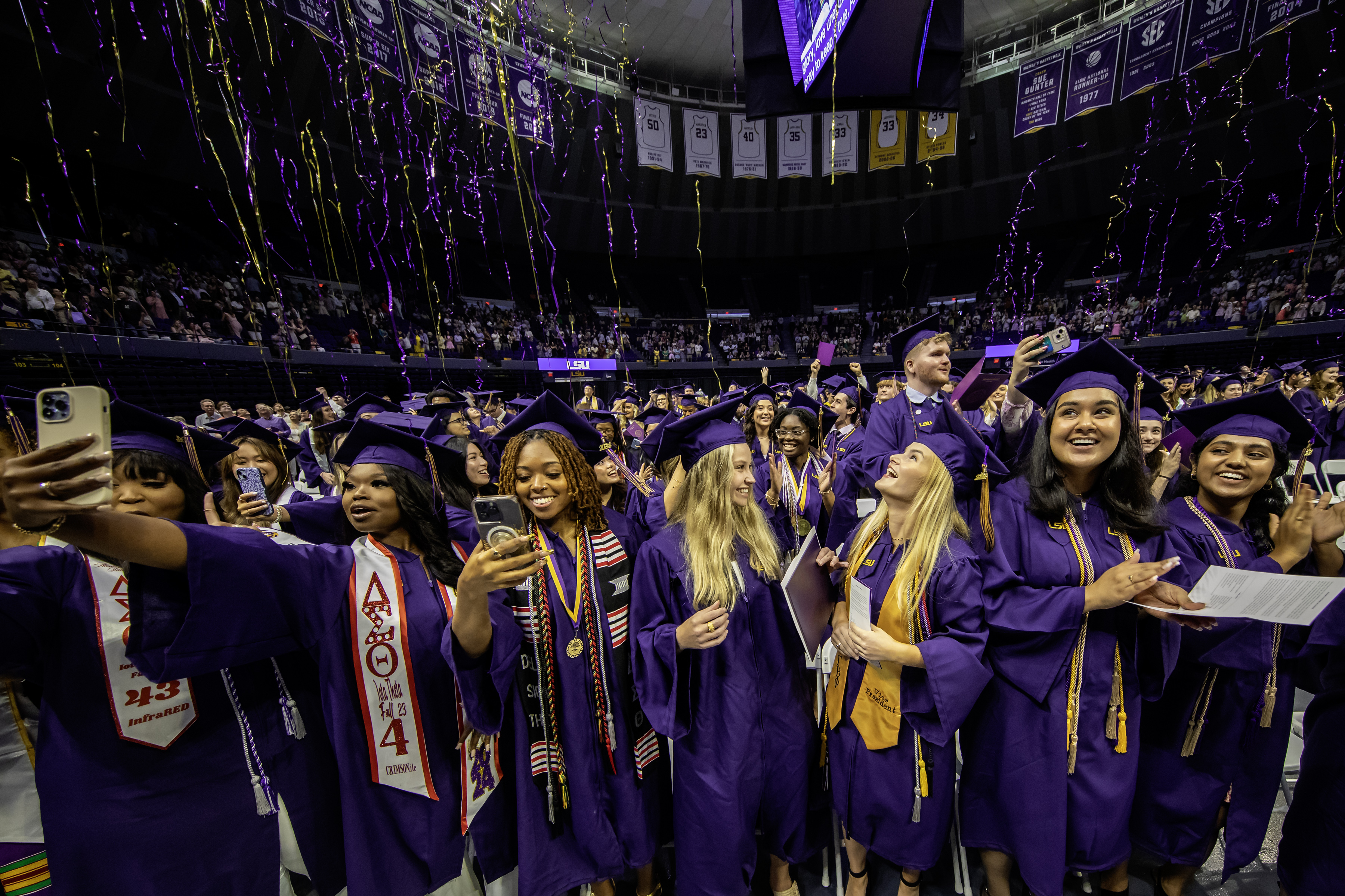 A group of graduates celebrates as streamers fall from the ceiling during commencement exercises.