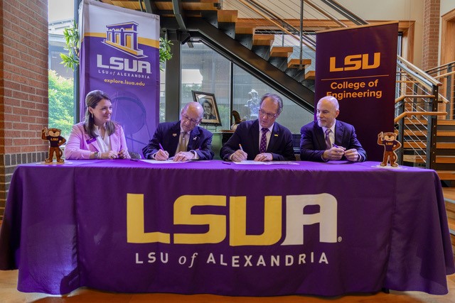 LSU Alexandria and LSU College of Engineering officials sign partnershhip documents at table draped with LSUA cloth sign with LSUA and LSU Engineer banners in the background