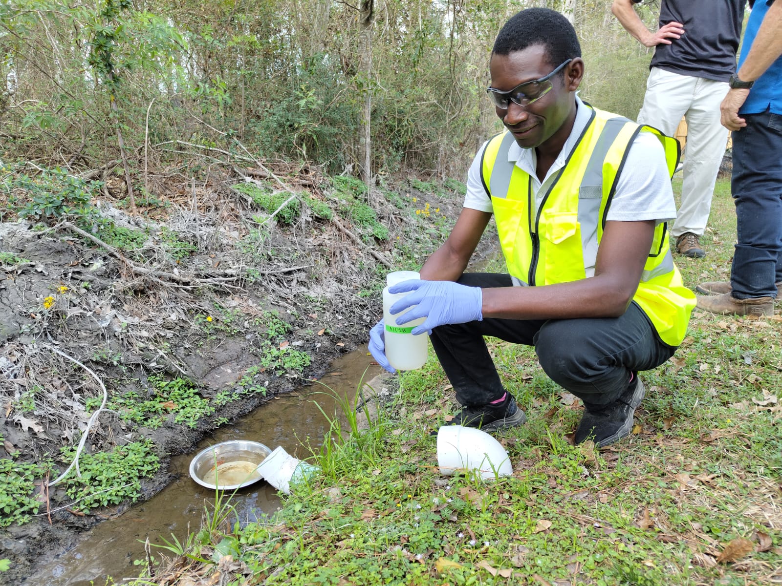 A student collects water samples from a shallow stream.