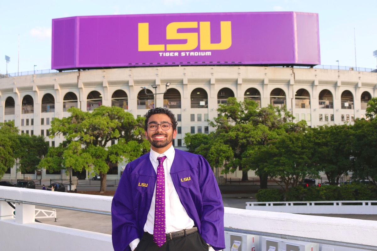 LSU graduate, Mihir Babbar, stands in front of Tiger Stadium wearing his graduation gown.