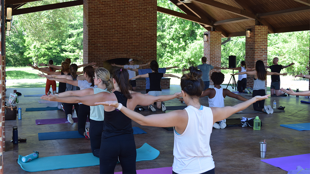 group of people do yoga stretches under open air pavilion