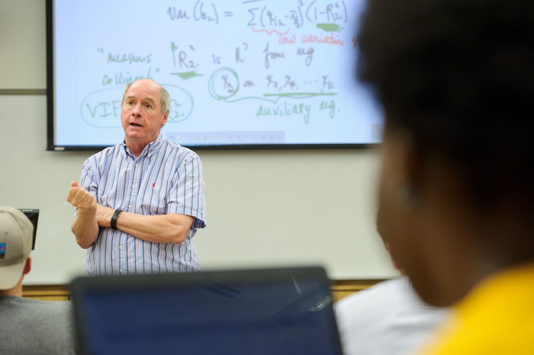 Professor teaches economics class with project in backgroun