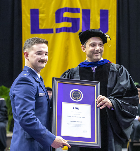 Austin Firmin receives a framed award from Dean Llorens on stage during the E. J. Ourso College of Business graduation ceremony.