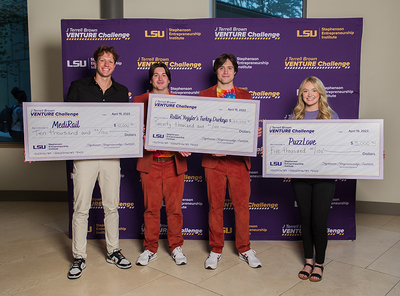 Student founders smile and hold large checks showing their winnings in the J Terrell Brown Venture Challenge