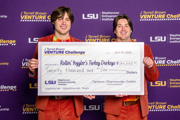 two men in orange suits hold large check for twenty thousand dollars