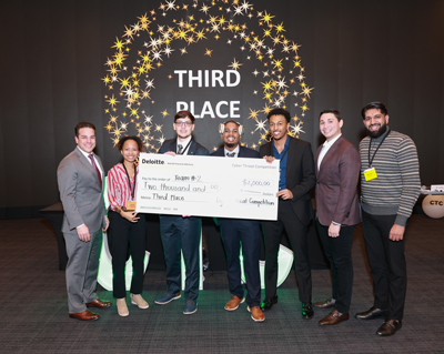 Photo of the team including Daniel Lichowid Jr holding a large check in front of a sign that reads third place