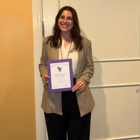Michael-Leah Hart wears professional attire and smiles while holding a certificate. 