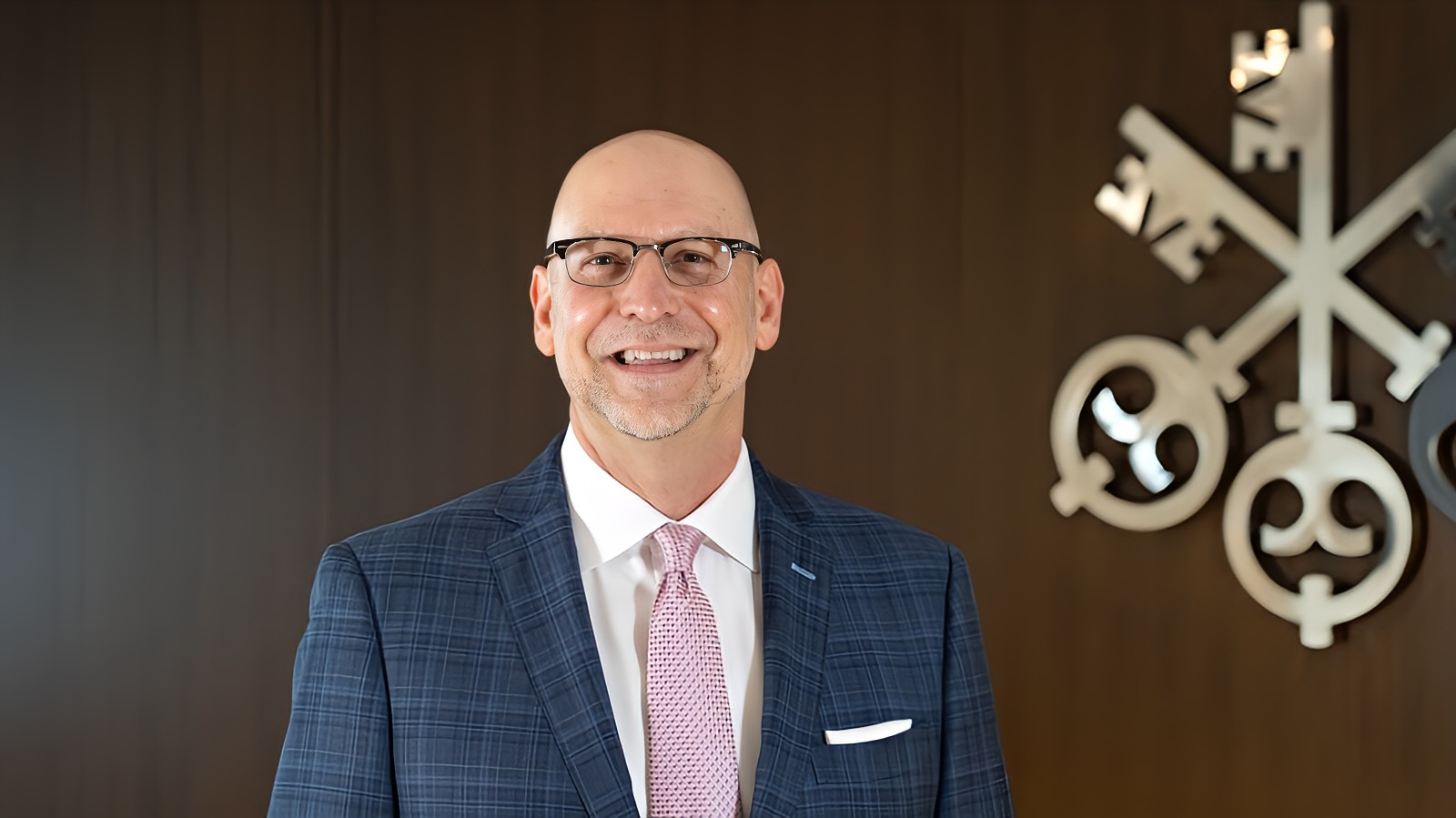 Patrick Evans wears a suit and stands in front of a wall with a large USB Financial Serices logo