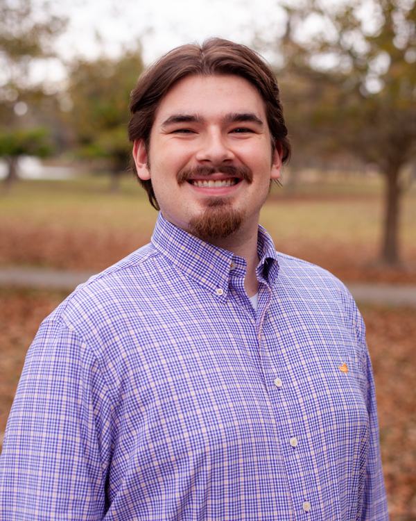 Matthew Rotolo's headshot was taken outdoors in the autumn. He smiles warmly while wearing a plaid dress shirt.