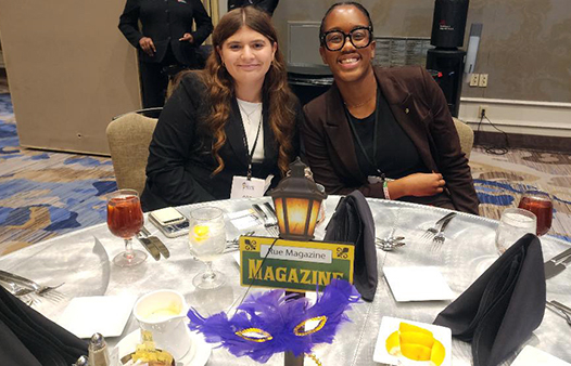 Two students in professional attire sit a table with New Orleans-themed decor
