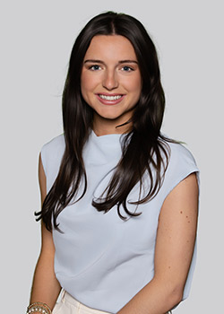 Vivian Ely wears a light blue blouse and white slacks in this headshot. She smiles at the camera.