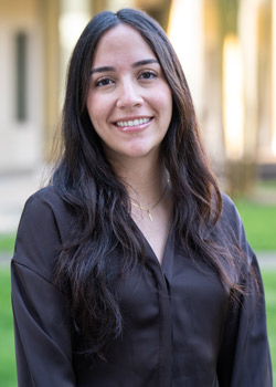Paola Rodriguez wears a black satin blouse and smiles as she stands in the BEC Courtyard.