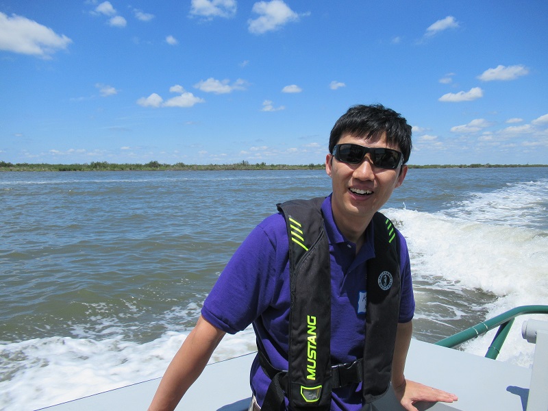 Kevin Xu in sunglasses and a lifevest smiles while on a boat on water
