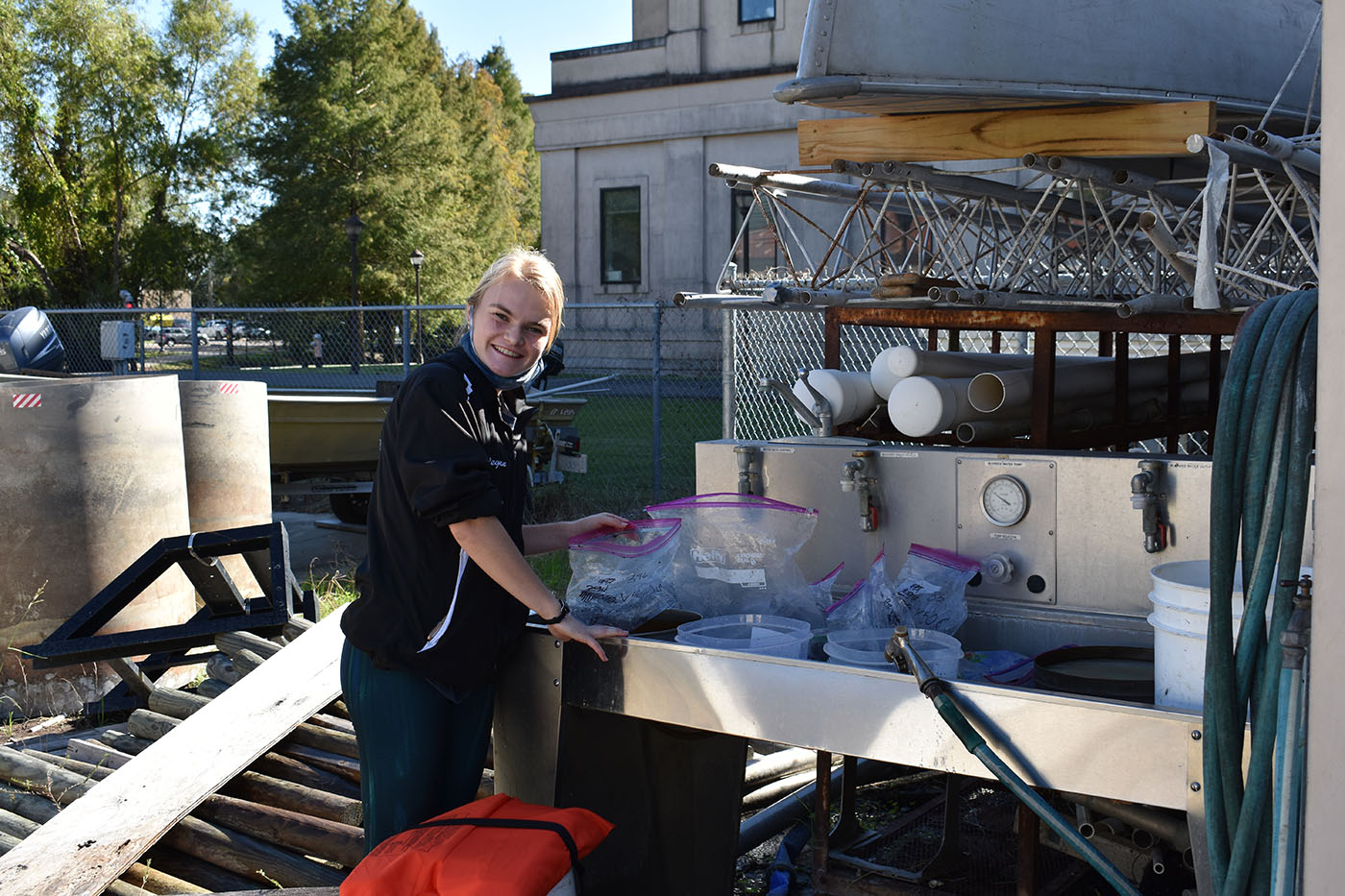 a woman stands with equipment in a boatyard