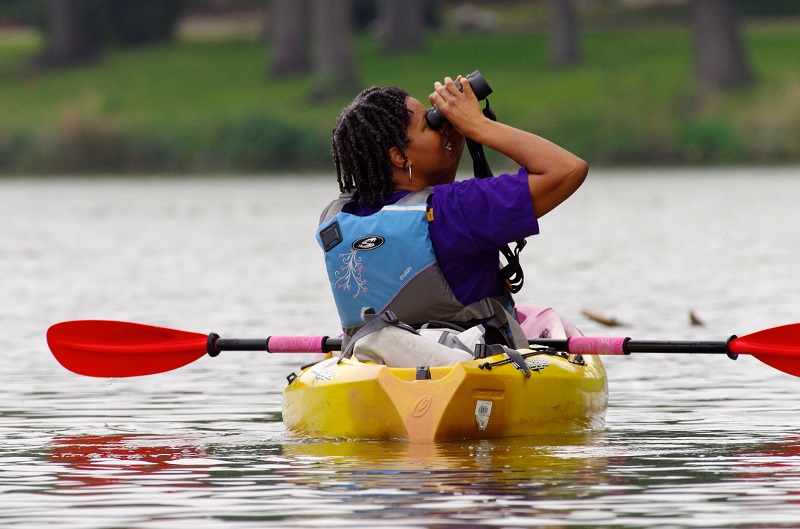 a woman on a kayak looks through binoculars