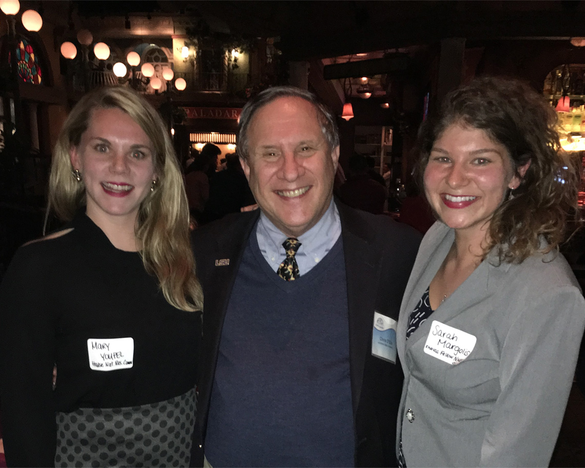 Three people in a bar wearing name tags smile at a camera