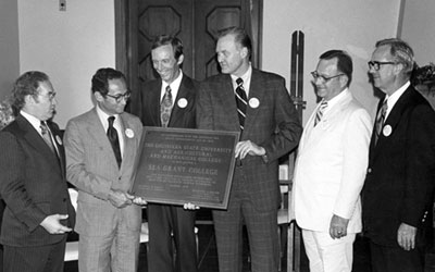 black and white photo of six men holding up a plaque