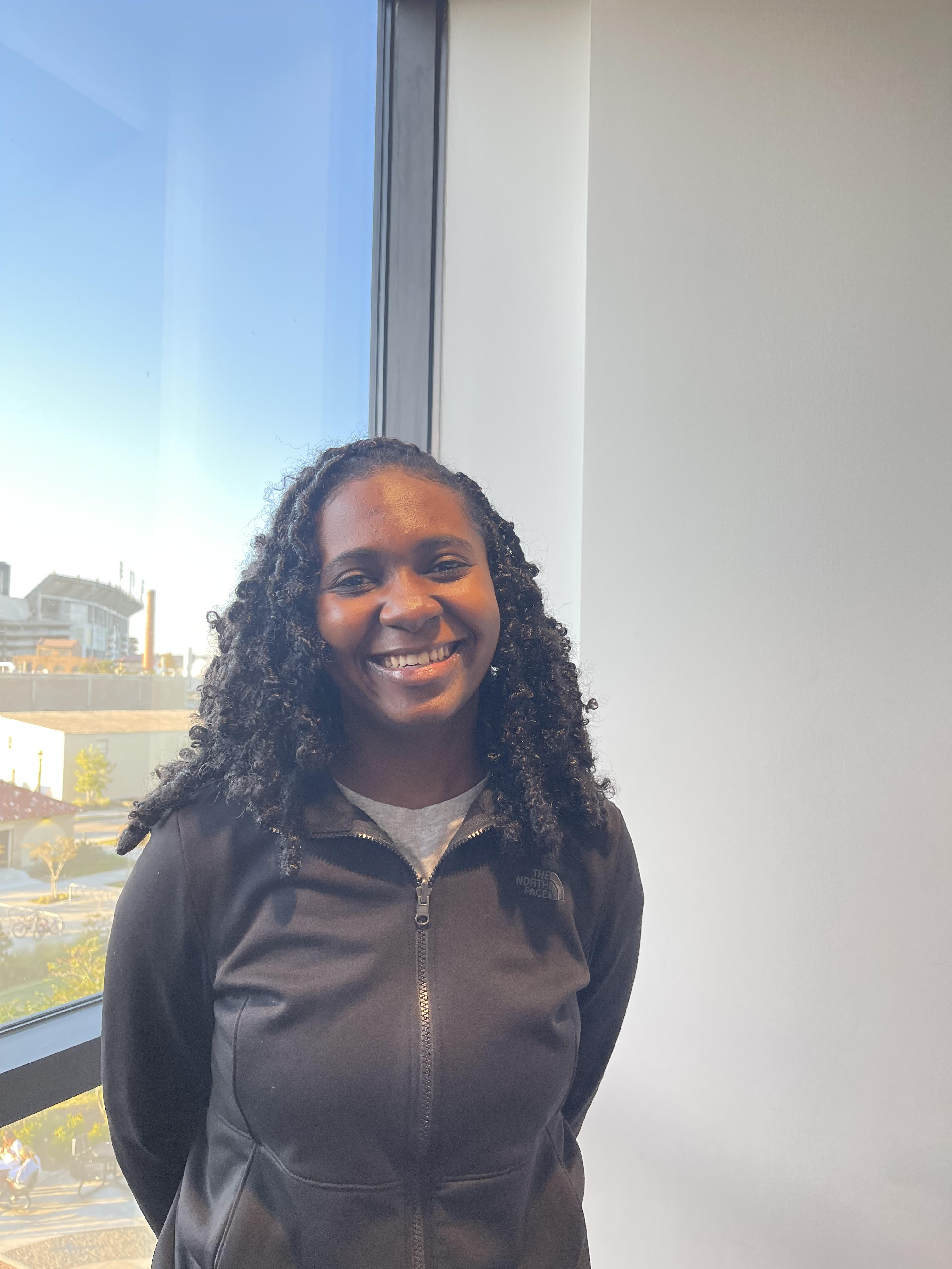 A woman stands in front of a window smiling