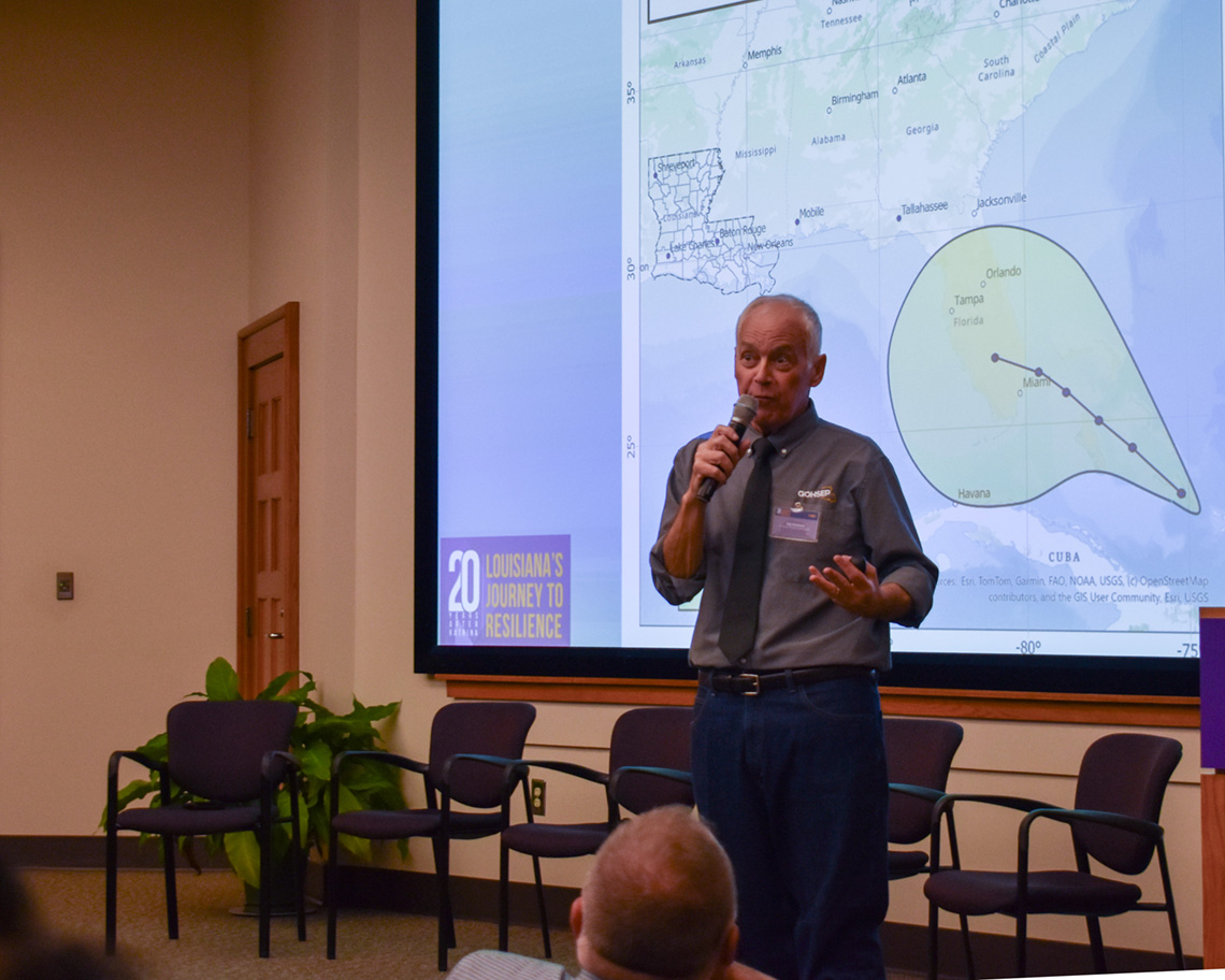 a man holds a microphone in front of a hurricane map