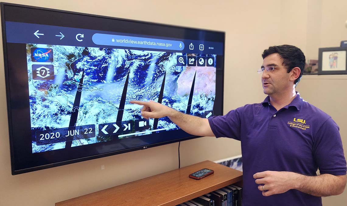 A man stands in front of a television with satellite imagery of the Earth on it