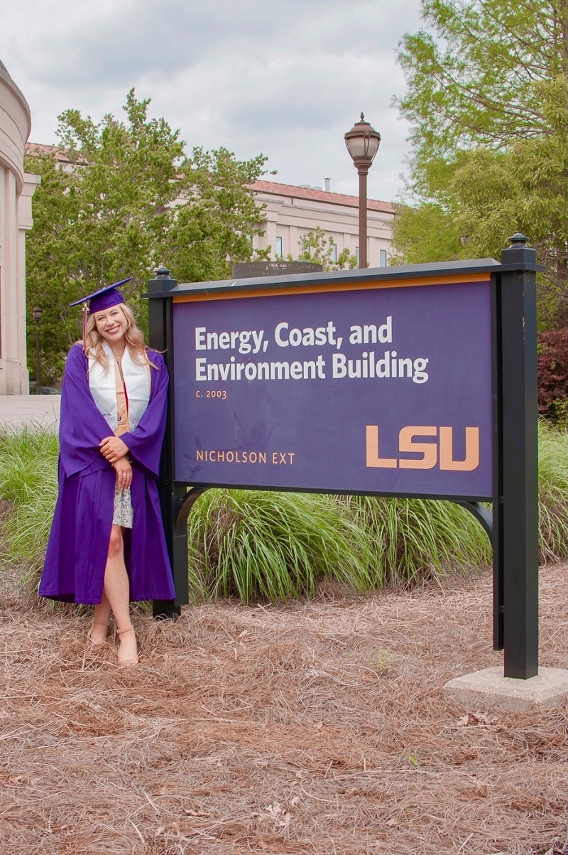 Simone Sale in a graduation cap and gown poses in front of the ECE Building sign