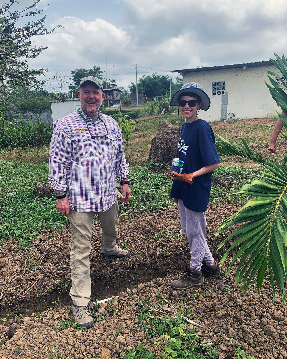 A man and a woman stand and smile with a shovel