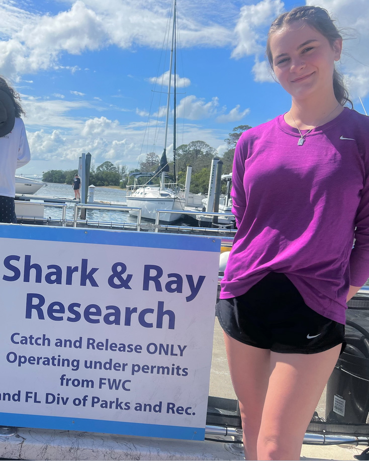 coastal environmental sciences student stands next to a sign