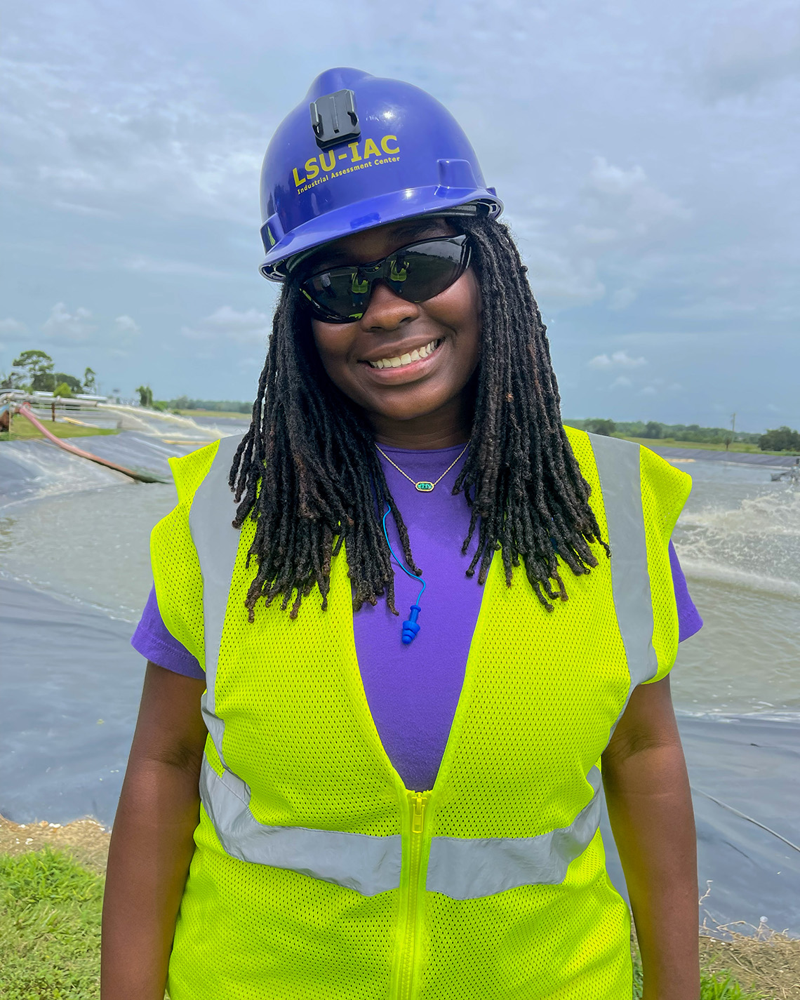 A woman wearing a hard hat and work vest smiles at the camera