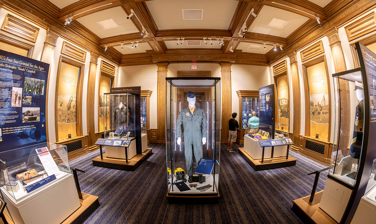 A museum exhibit room with wooden beams on the ceiling, display cases featuring historical artifacts, and a central glass case containing a military uniform and related items. Description generated by AI