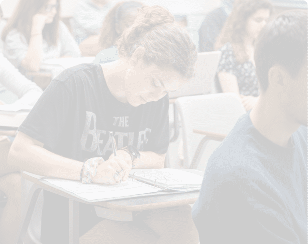 Three people sit at a table with books, a whiteboard with words written on it, and markers, engaged in a learning or teaching activity. Description generated by AI