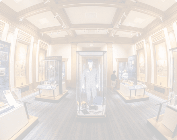 A museum room with wooden paneling and display cases featuring historical clothing and informational panels, with two people observing the exhibits. Description generated by AI