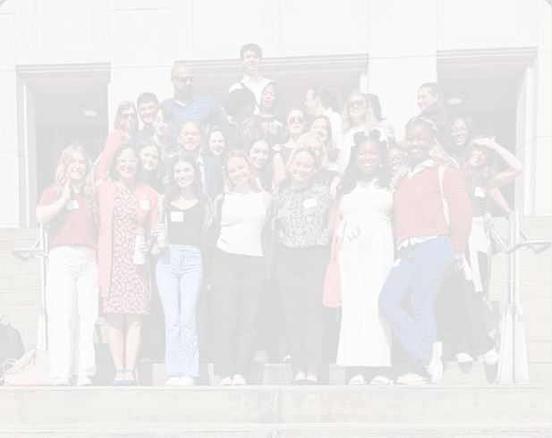A group of adults dressed in casual and semi-formal clothing are standing on outdoor steps, smiling and posing for a group photo in front of a building. Description generated by AI