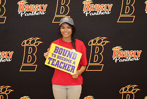 Photo of Daija Grimes wearing an LSU hat and standing in front of a Brusly High School Backdrop