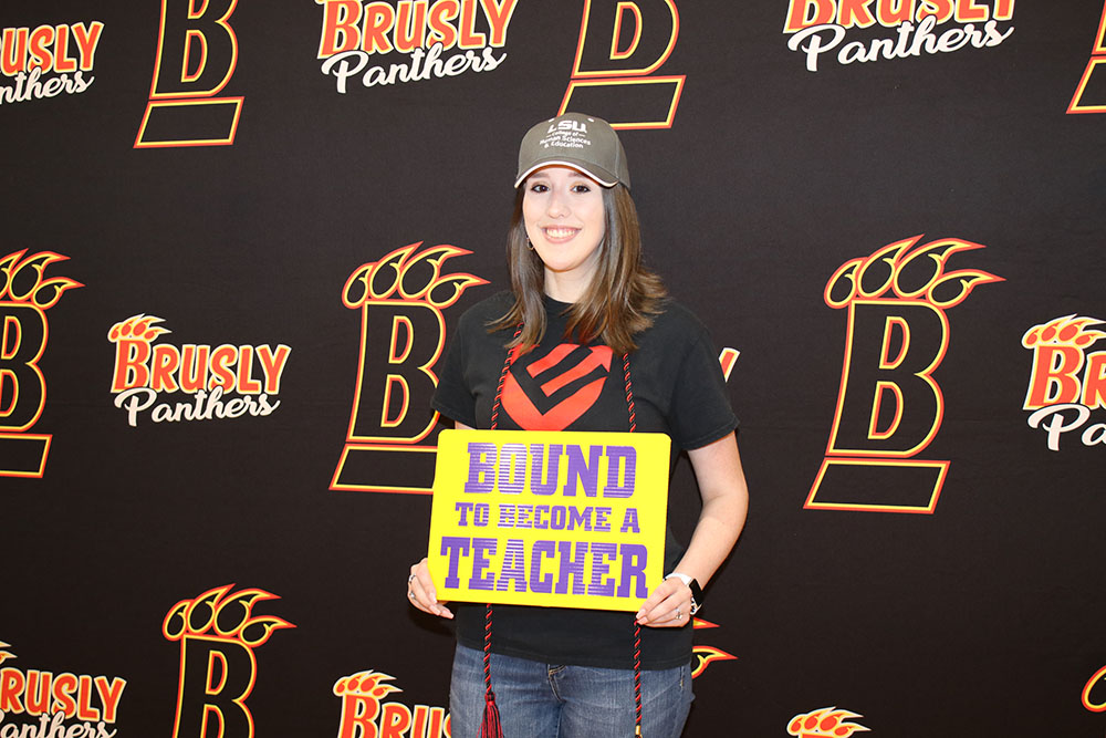 Photo of Olivia Stearns wearing an LSU hat and standing in front of a Brusly High School Backdrop