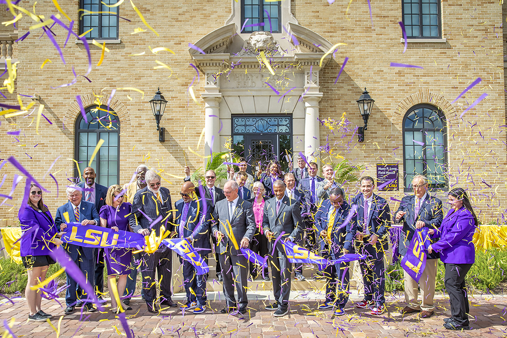 purple and gold confetti and men and women cutting a purple ribbon in front of the Huey P. Long Field House