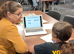 Tutor works with a young student on a word-reading activity using a laptop.
