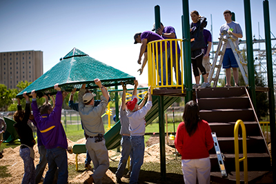 CPP playground volunteers lifting a roof to other volunteers standing on an elevated platform of a piece of playground equipment