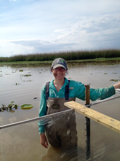 Kathleen Eubanks wearing chest waders stands in the thigh-deep water of a marsh