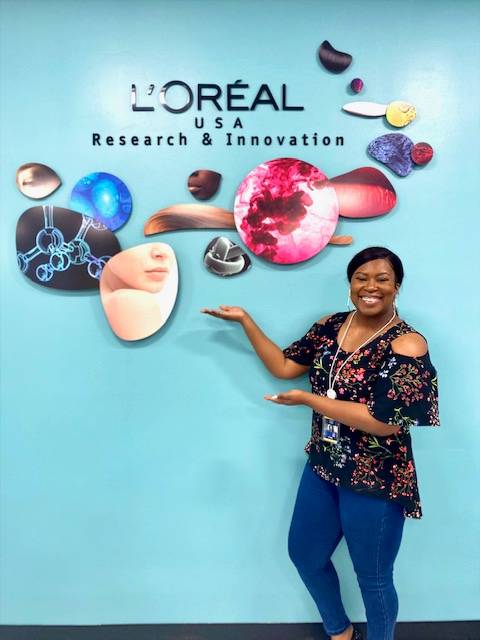 Ololade "Lola" Adeola standing in front of L'Oreal logo on wall