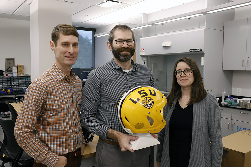Andrew Becnel, Hunter Gilbert and Genevieve Palardy holding a football helmet