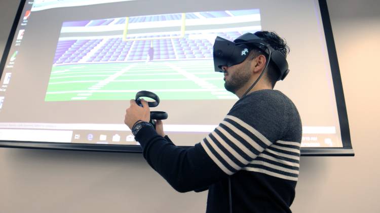Man with virtual reality goggles on in front of screen